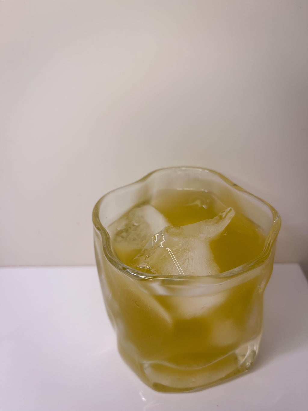 Glass of yellow liquid with ice cubes on a white surface