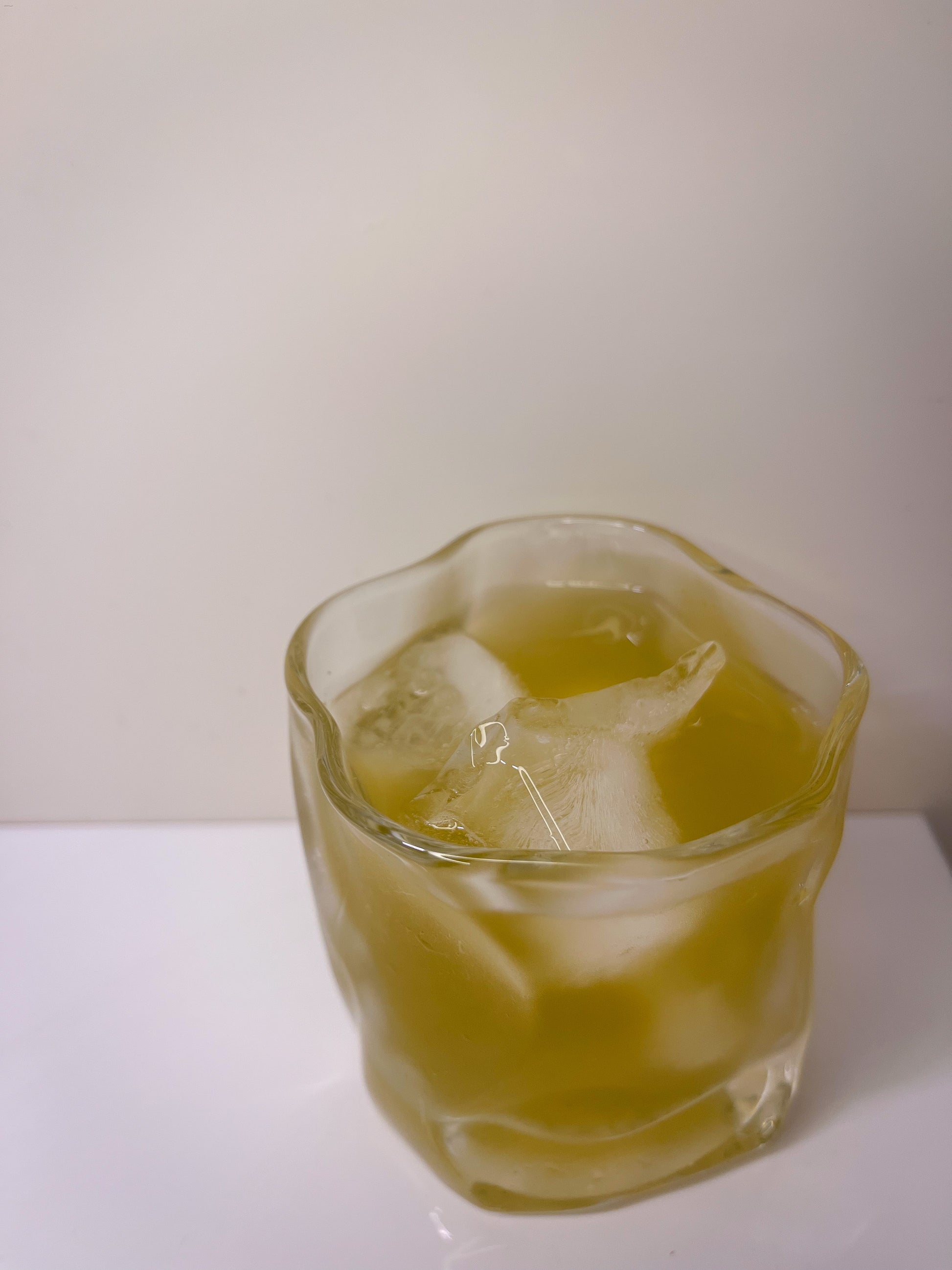 Glass of yellow liquid with ice cubes on a white surface